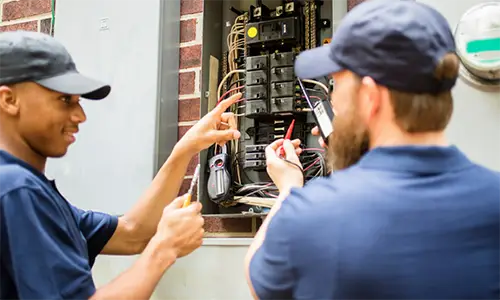 Electricians inspecting and testing a residential electrical panel during rewiring and breaker replacement service.