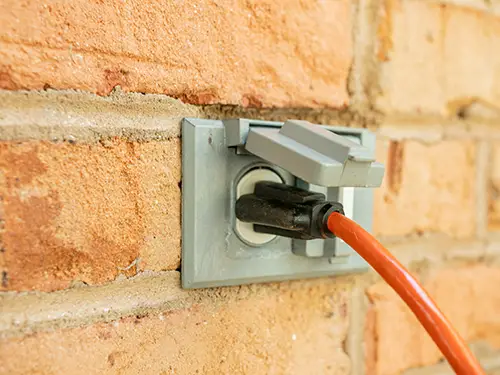 Weatherproof exterior electrical outlet with outdoor power cord plugged in