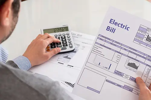 Homeowner reviewing an electric bill and calculating energy costs with a calculator